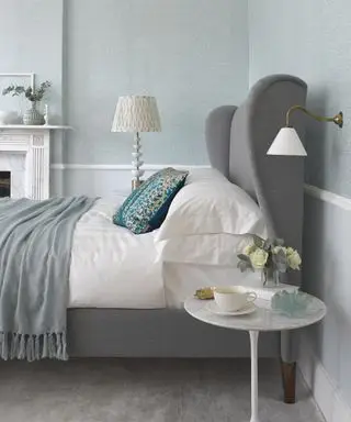 Un exemple de planification de l'éclairage d'une chambre montrant un lit gris avec une lampe de chevet blanche et une applique blanche et dorée