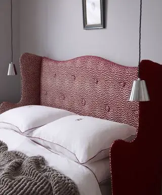 Gros plan d'un lit avec une tête de lit en relief rouge et blanc avec une literie blanche et deux lampes suspendues
