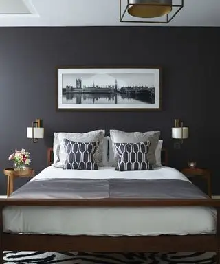 En grå soveromside med mørke vegger, hvitt lin og svart tilbehør