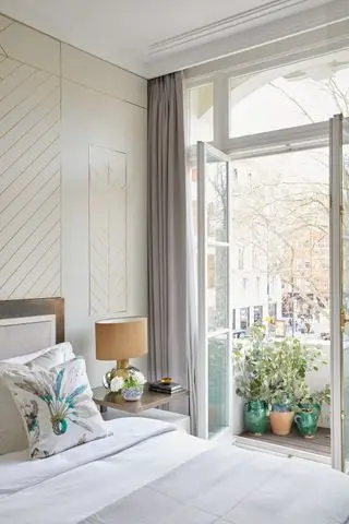 chambre neutre avec mur en pierre avec incrustations dorées, literie blanche, lampe ocre, vue sur le balcon