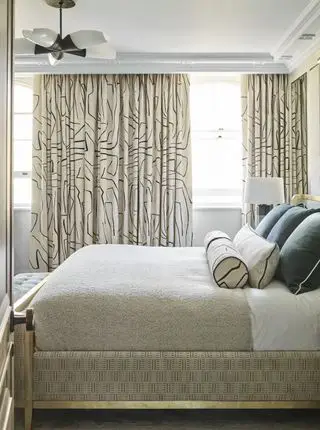 chambre neutre avec rideaux à imprimé linéaire, lit bordé d'or, oreillers bleu sarcelle, couverture taupe, suspension