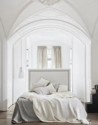 chambre blanche avec literie grise et neutre, rideaux à la fenêtre, plafond voûté, parquet