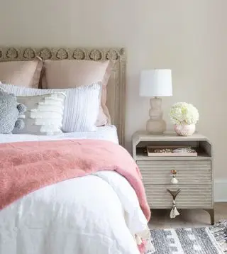 chambre neutre avec des accents corail, tête de lit et table d'appoint texturées, tapis texturé gris, murs en pierre