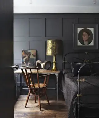 Une chambre avec des murs lambrissés peints en noir, un plafond blanc et du parquet