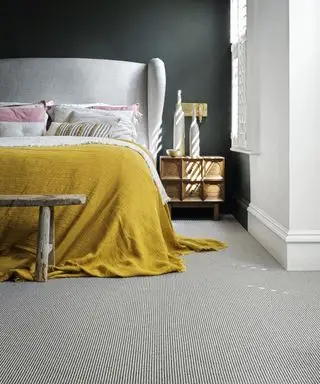 Une chambre aux murs noirs, un lit blanc avec un jeté jaune et un tapis à rayures noires et blanches