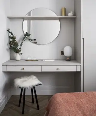 Et soverom med innebygd sminkebord, sirkulært speil og fluffy sete