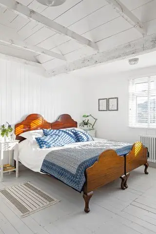 Dormitorio blanco con paneles traslapados, suelo de madera gris y una cama de madera.