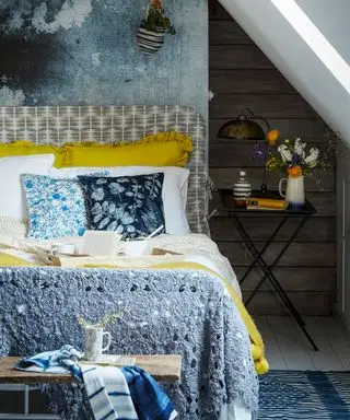 Un lit avec une tête de lit à motifs gris et blancs et une literie jaune à côté d'une table de chevet noire