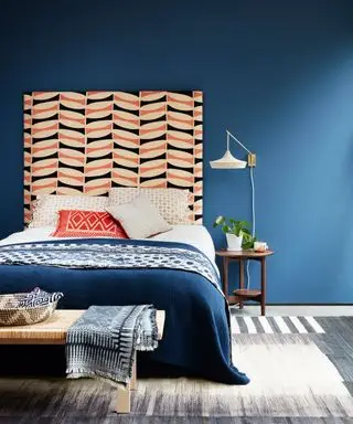 Un exemple d'idées de chambre montrant un mur bleu derrière un lit avec une tête de lit orange et blanche et une applique blanche