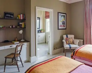 Une chambre d'amis qui fait également office de bureau avec des plaids orange sur les lits