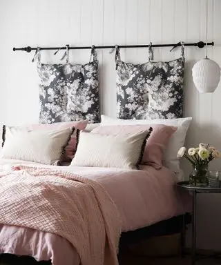 Un exemple d'idées de chambre d'amis montrant un lit avec une literie et des coussins roses, ainsi qu'une tête de lit composée de coussins suspendus.
