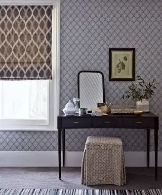 Une coiffeuse en bois avec un tabouret rembourré devant du papier peint à motifs