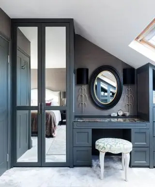 Une chambre avec une armoire grise et une coiffeuse avec un tabouret