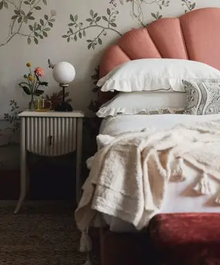 Un lit rose avec une literie blanche devant un papier peint fleuri