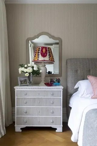 石と青の壁紙が付いたベッドルーム、グレーの布張りのベッド、ヴィンテージのベッドサイド、模様のあるランプシェード、木製の床