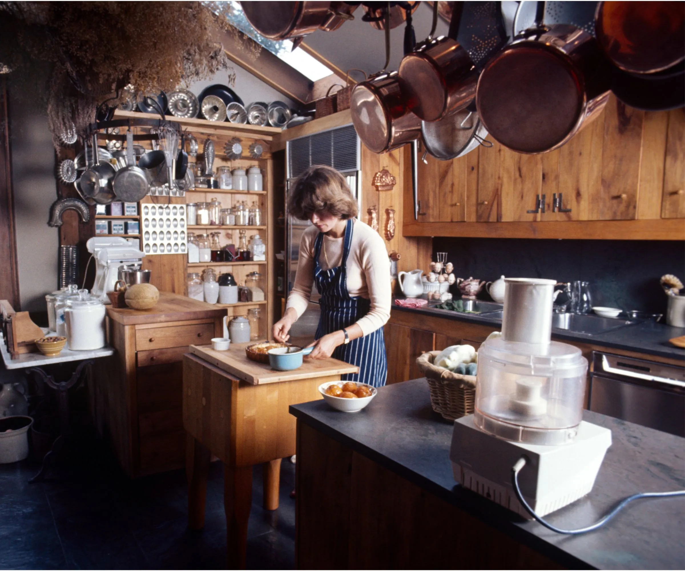 Martha Stewart dans sa cuisine de ferme avec armoires de cuisine en bois, casseroles en cuivre accrochées au garde-manger avec bocaux et moules en cuivre' loading='lazy' title=