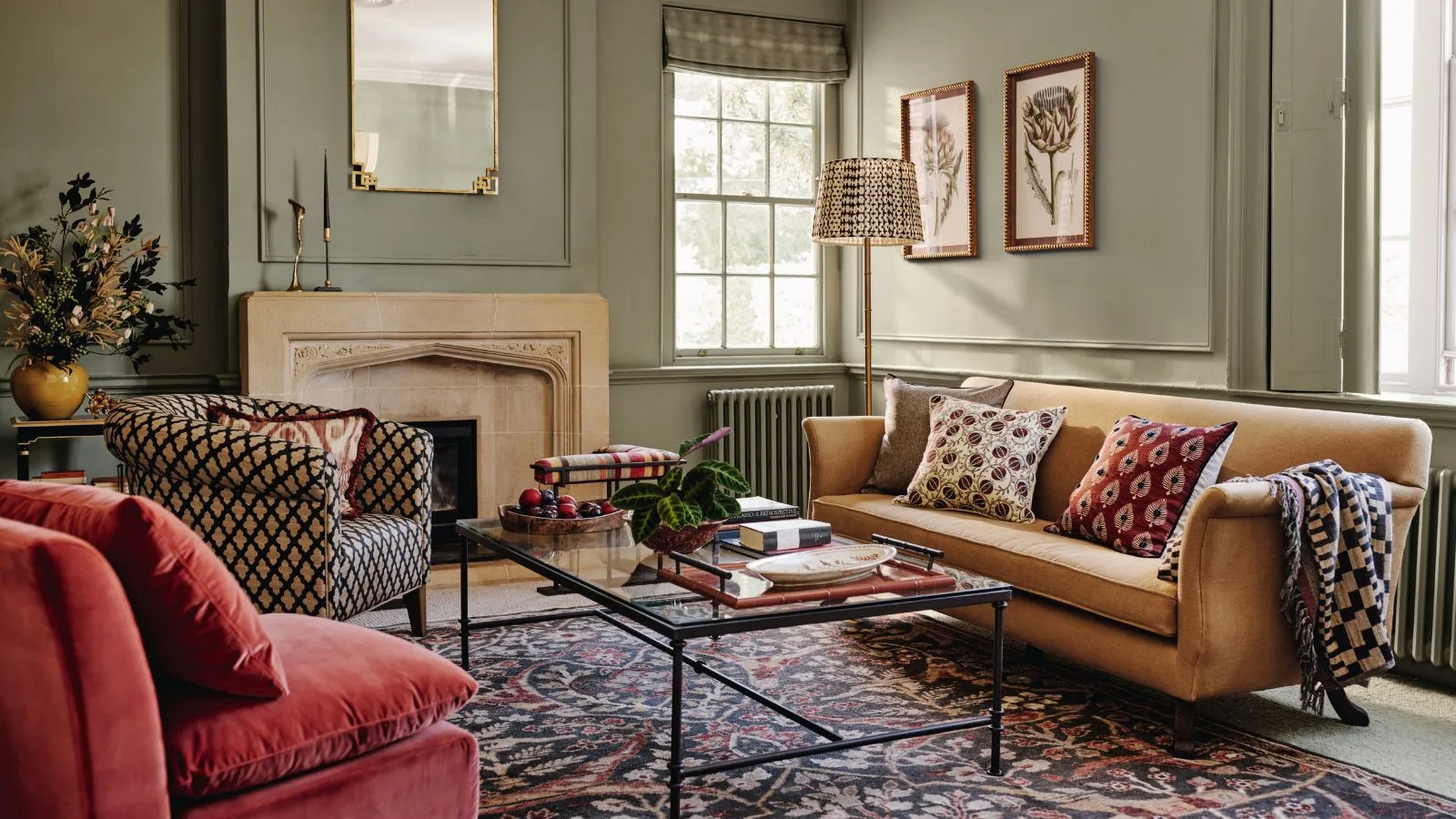 Zelená obývačka so žltou pohovkou, červeným kreslom a vzorovaným kreslom okolo skleneného konferenčného stolíka pred kamenným krbom.' loading='lazy' title=