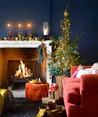 Salon confortable avec cheminée et feu allumé, canapé et repose-pieds orange, arbre de Noël décoré d'ornements colorés