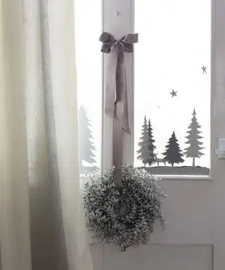 Ideias de decoração de janelas de Natal com árvores cinza e brancas e adesivos de floco de neve no painel da janela de uma porta branca