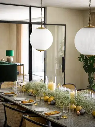 Salle à manger de Noël avec table dressée, guirlande de gypsophile, bougies ouragan, boules d'or et couverts
