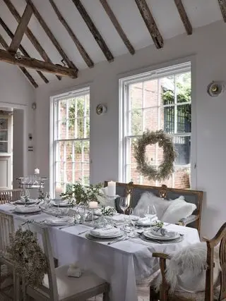 Salle à manger de Noël blanche avec décors festifs, guirlande de perles, couronnes intérieures, banquettes et chaises de salle à manger