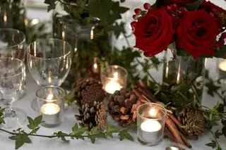 Table de fête avec vases de roses rouges et de baies, pommes de pin, bâtons de cannelle, guirlande de feuillage