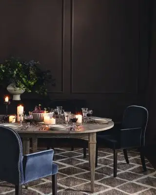 salle à manger avec murs en chocolat noir, chaises bleu marine, décoration de table de style automnal, assiettes noires et blanches, bougies, vase de fleurs et de baies