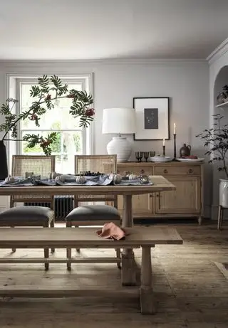 spisebord med grå løper og sølvgresskar, telys i sort glass, bærgren i høy vase, sittebenk og stoler, stor hvit bordlampe på skjenk