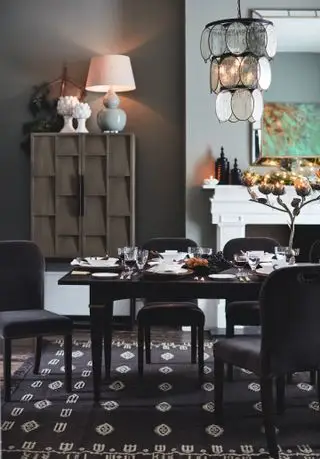 salle à manger aux murs gris, cheminée, grand garçon, lampe de table, suspension, table noire, chaises rembourrées grises, tapis noir