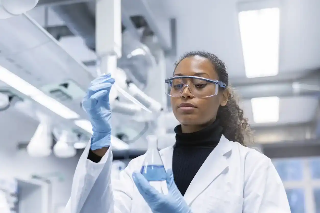 Woman scientist experimenting with chemicals in lab. Lab technician doing research on new chemicals in laboratory, adding solution in conical flask.
