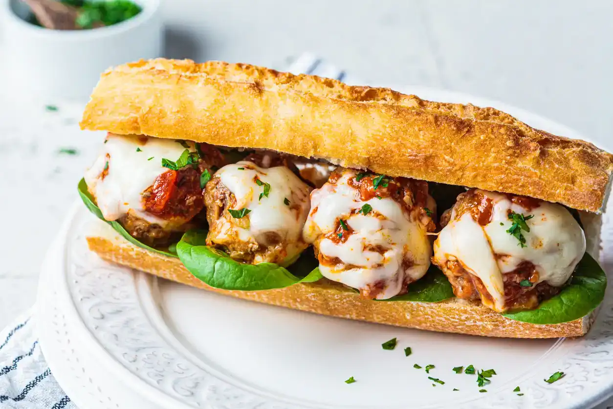 Sub Meatballs sandwich with cheese and tomato sauce in a baguette on a white plate