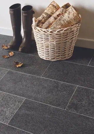 gros plan sur un sol en granit foncé dans le couloir avec des bottes et un panier à bûches