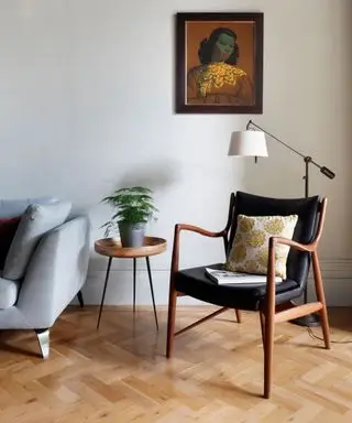 Poltrona com piso em parquet com parede cinza claro e sofá.