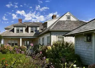 Ideias verdejantes de canteiros de flores no jardim da frente em torno de uma tradicional casa de madeira com janelas de empena.
