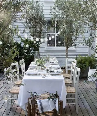 흰색 테이블보로 덮인 테이블과 스트링 조명 아래 등나무 의자가 놓인 의자가 있는 야외 식사 공간