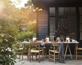 가을 테이블 장식과 회색 담요를 갖춘 검은색 목재 패널 하우스 외부에 나무 테이블과 의자를 갖춘 야외 식사 아이디어