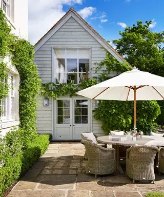 나뭇잎이 있는 백악관 앞에 등나무 의자와 흰색 파라솔이 있는 둥근 야외 식탁