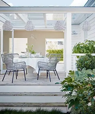 흰색 랜턴과 흰색 등나무 의자가 있는 정원 공간의 흰색 야외 식사 공간