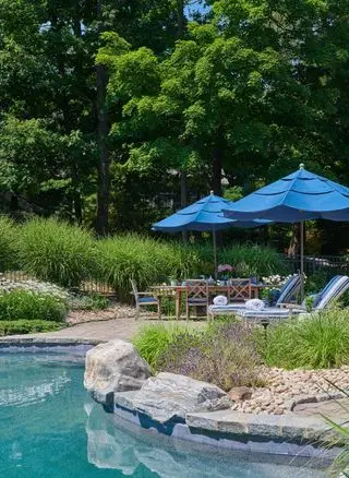 Terrasse neben dem Pool mit Liegen, Tisch, Stühlen und Sonnenschirm