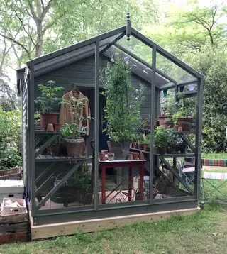 Un hangar gris foncé avec une extension de serre remplie de plantes en pot.