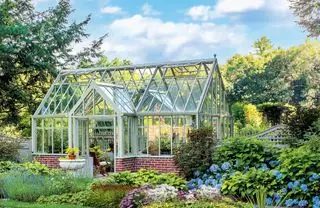 Idées de serres traditionnelles avec un petit socle mural en briques, dans un jardin luxuriant avec des hortensias bleus.