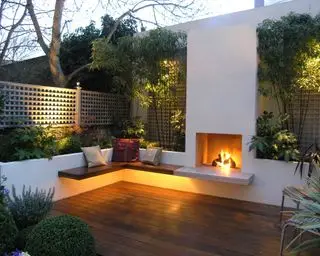 petit patio avec terrasse en bois, foyer extérieur, sièges et lits surélevés avec bambou éclairé