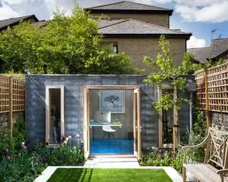 Ein Gartenzimmer am Ende eines einsehbaren schmalen Gartens mit Rasen, Spalier und einer Holzbank.