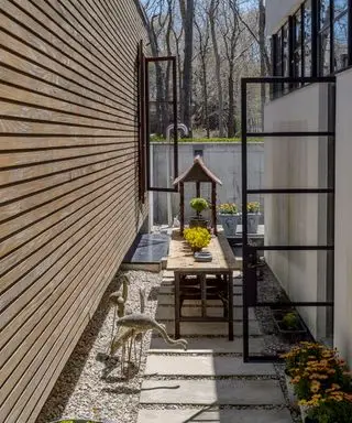 Ein Beispiel für kleine Hinterhofideen, das einen kleinen Innenhofbereich mit Vogelstatuen, Pflastersteinen und einem schmalen Tisch zeigt