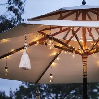 Un exemple d'idées d'éclairage à cordes extérieures montrant un parasol de jardin avec des guirlandes lumineuses