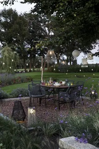 Un patio en gravier avec une table à manger, des chaises et des guirlandes lumineuses