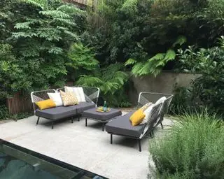 petite cour-jardin avec coin salon en terrasse et plantations à feuilles persistantes