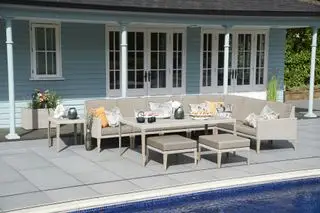 Großes Sofagarnitur auf der Außenterrasse zwischen einem hellblauen Haus, einer Veranda und einem Pool.