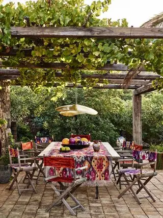 Terrassentisch und Stühle im Boho-Stil unter einer rustikalen Pergola mit Weinreben.