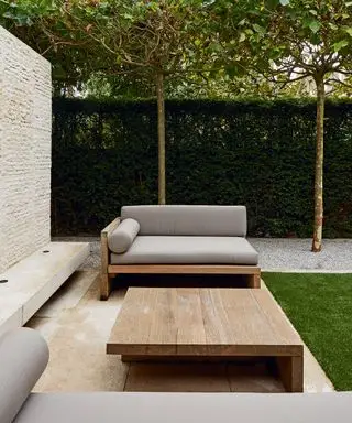 Minimalistische Ideen für Terrassenmöbel für den Außenbereich mit eleganten Holzmöbeln und gepflegten Buchsbaumhecken und Bäumen dahinter.